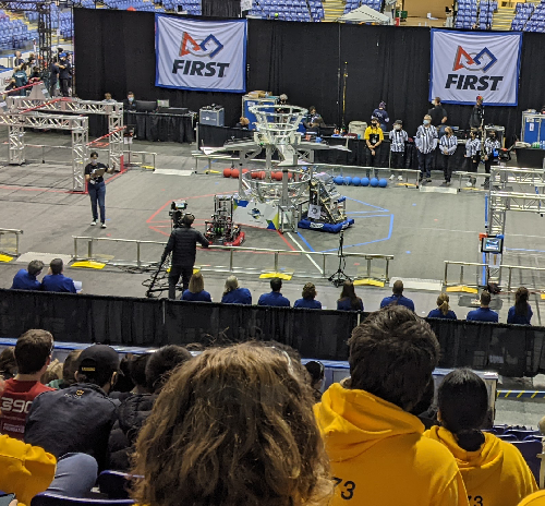 A stage with the FIRST robotics logo and 3 robots in competition